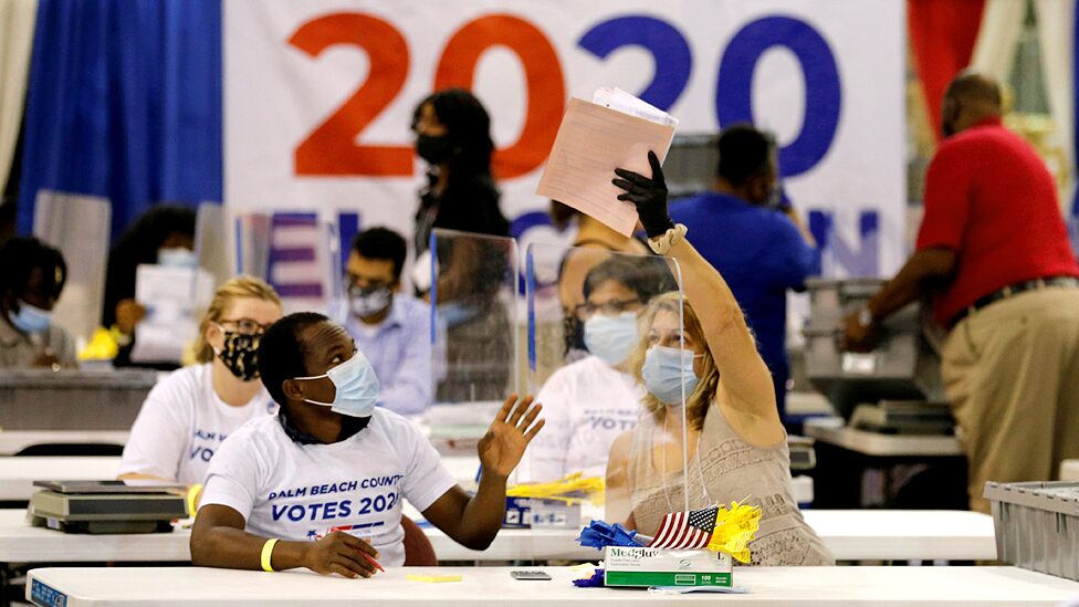 A poll worker passes paper to another worker on a plastic screen