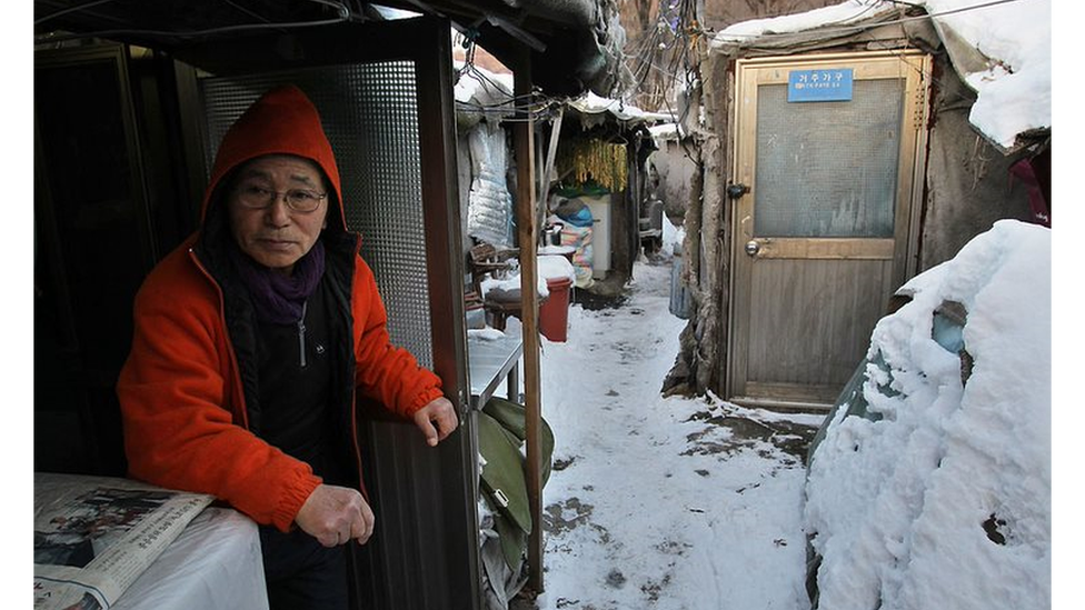 An elderly South Korean man sitting in Seoul's Guryong slum with snow on the ground