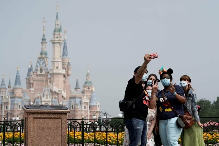 Visitors wearing protective face masks pose for a picture at Shanghai Disney Resort as the Shanghai Disneyland