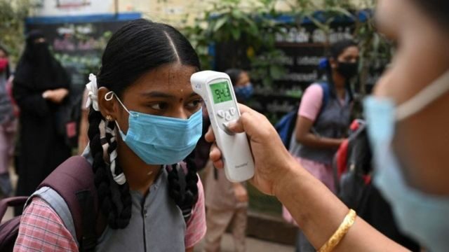 A teacher checks the temperature of a girl as she arrives to attend classes after the reopening of schools closed as a preventive measure to curb the spread of the Covid-19 coronavirus, at a school in Madurai on February 01, 2022. (